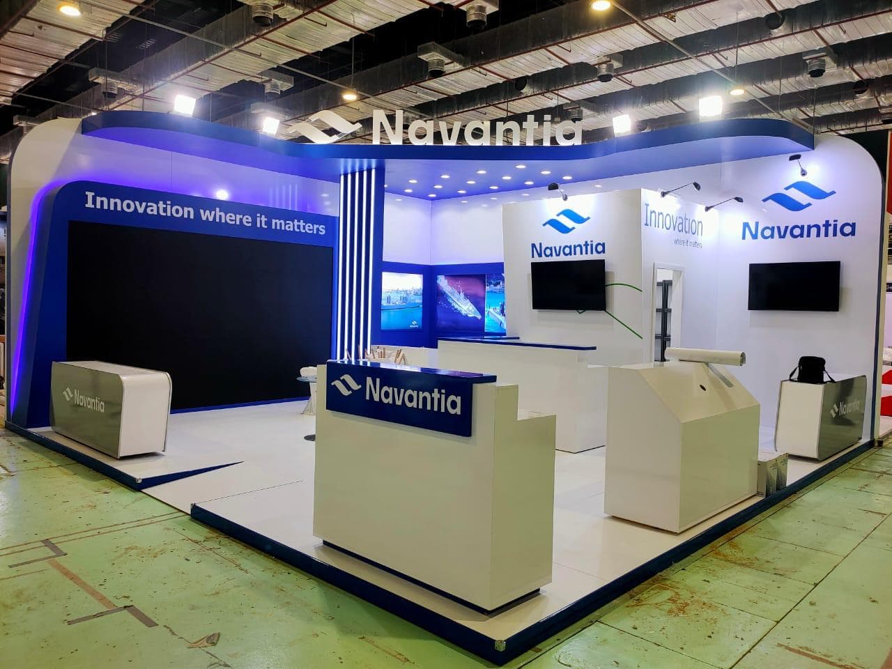 Backlit vertical fin façade under blue-wash lighting, Equal's stand for Navantia